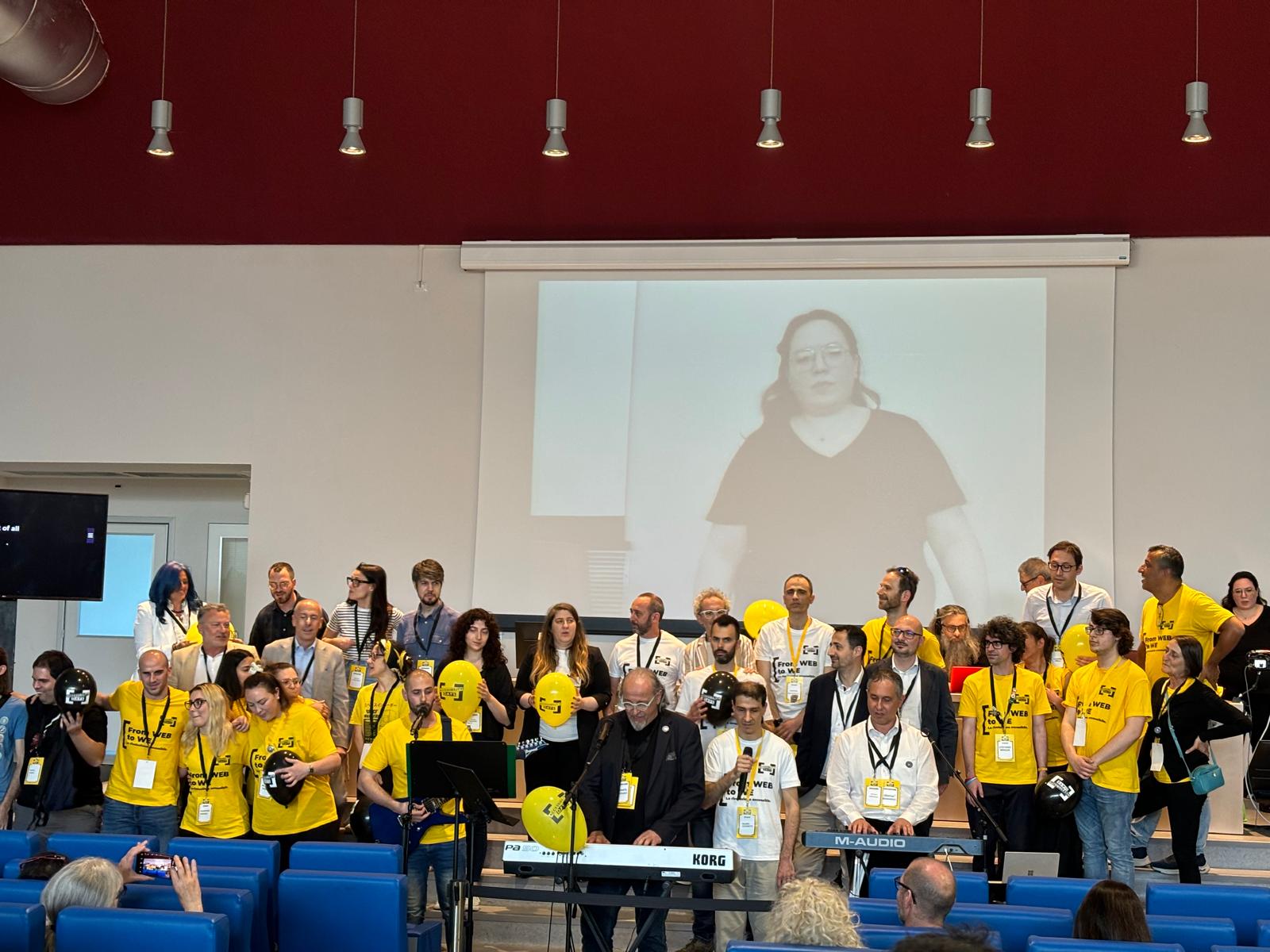 Organizzatori e relatori degli Accessibility Days 2024 cantano "We are the world" durante la chiusura dell'evento